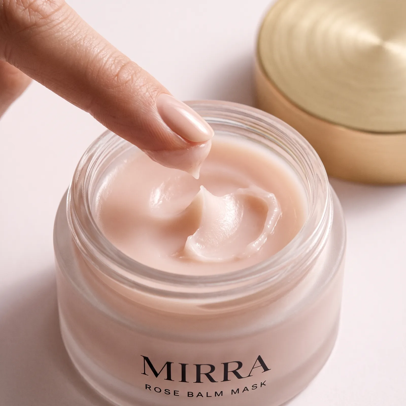A fingertip lifting a soft peak of rose balm